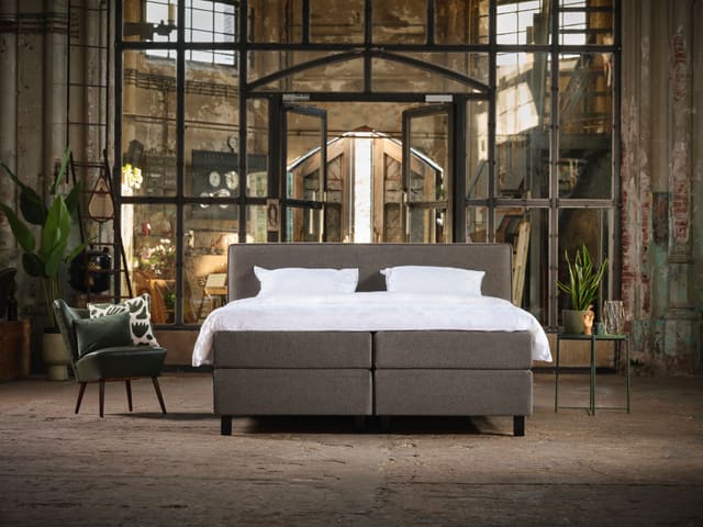 Boxspring met wit beddengoed in een lichte, industriële ruimte